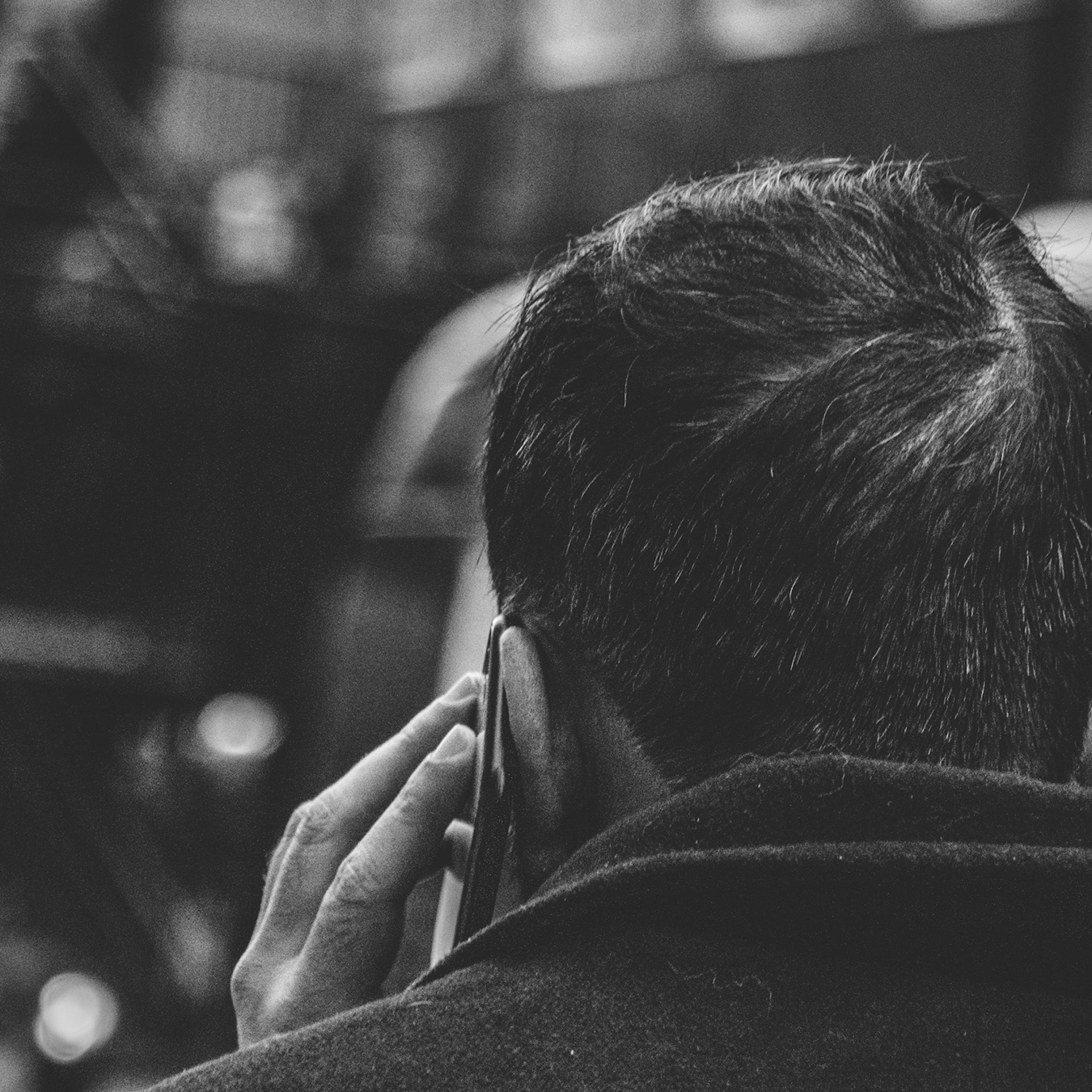 Dark-haired Man Wearing a Coat and Facing Forward with a Cell Phone at his Left Ear
