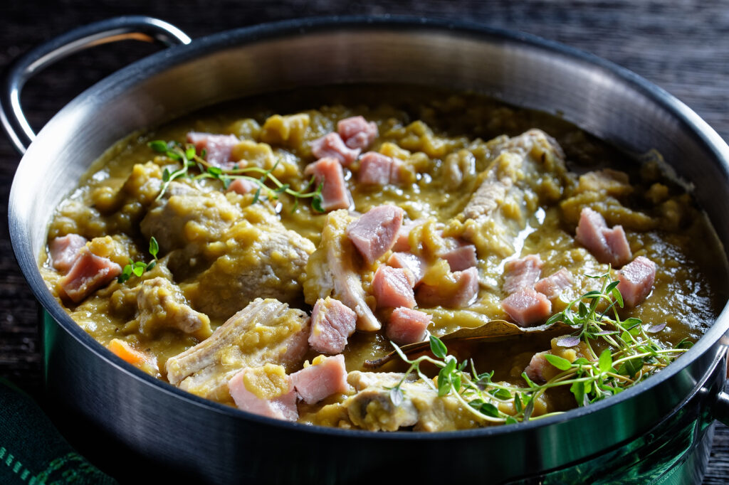 Photo of green pea soup with fresh herbs and ham in a pot.